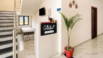 A hotel reception area with a marble staircase, a reception desk, a potted plant, and a wall-mounted sign.