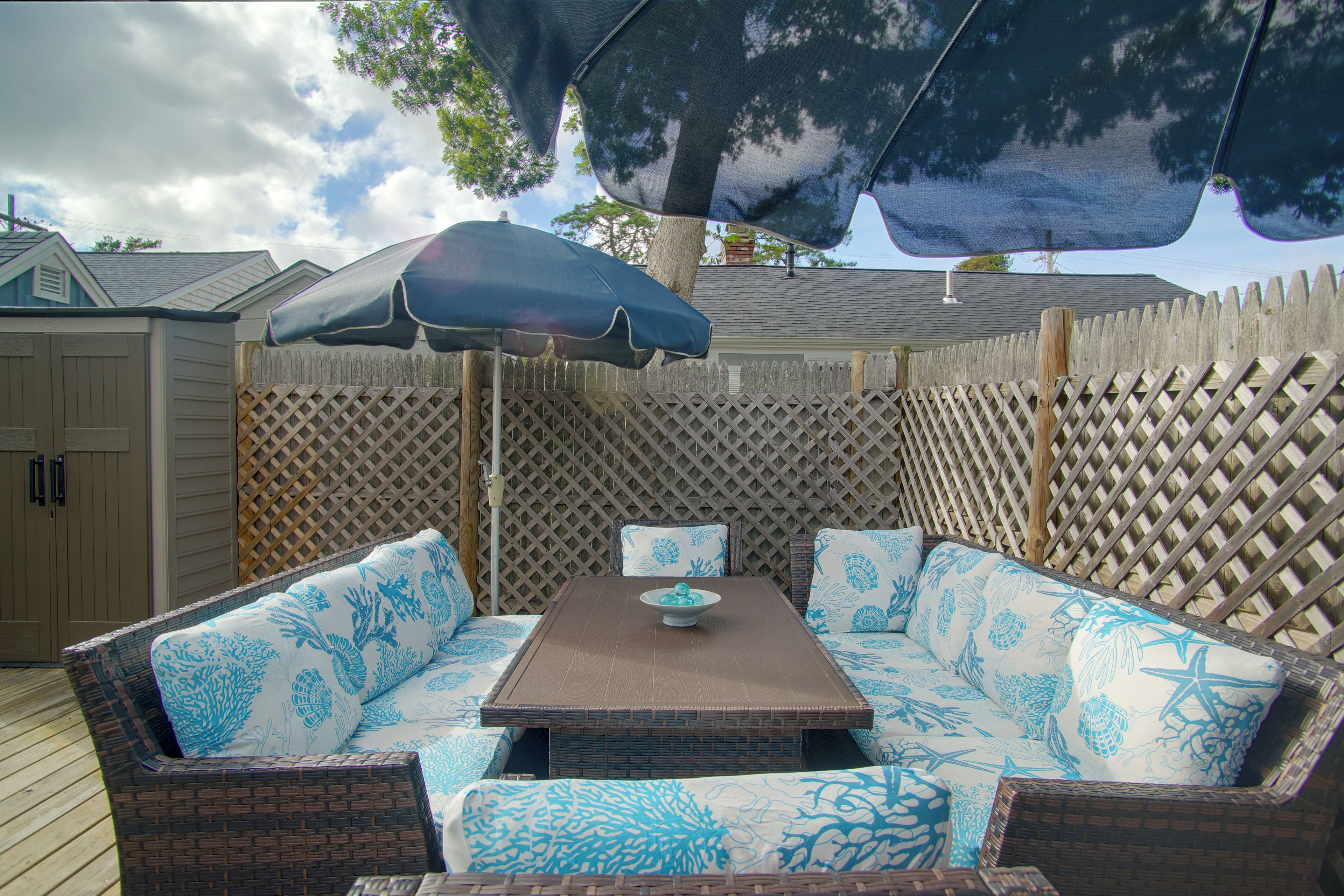 An outdoor patio with a wooden table and blue patterned sofa.