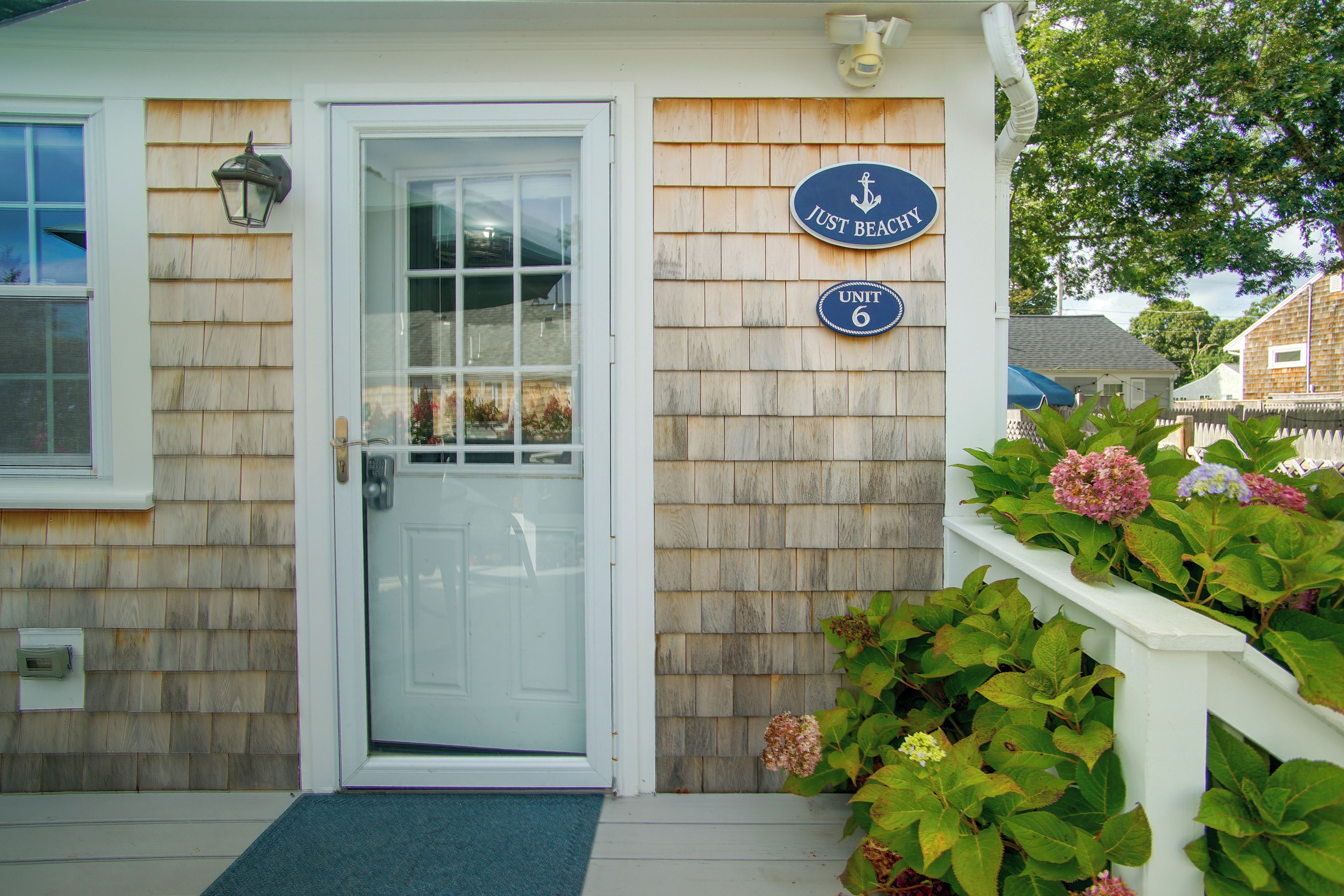 A wooden house with a white door, a 'Just Beachy' sign, and a 'Unit 6' sign.