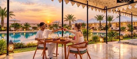 A couple dining at a table with a pool view, under a canopy with star patterns, at Grand Marusthal Resort.