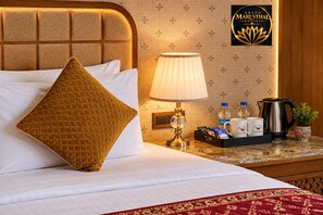 Una habitación de hotel con una cama, una mesita de noche, una lámpara, una bandeja con tazas y una tetera, y un cartel para Grand Marusthal Resort.