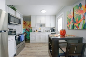 A modern kitchen with white cabinetry, a built-in oven, and a dining area with a table and chairs. - Walk to MBTA Station! Gloucester Extended Stay (Gloucester)