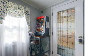 A room with a slot machine, a chair, a door with a decorative glass panel, and sheer curtains. - Walk to MBTA Station! Gloucester Extended Stay (Gloucester)