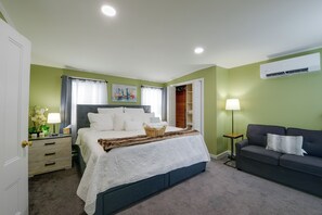 A hotel room with a bed, a sofa, a nightstand, a lamp, and an air conditioning unit. - Walk to MBTA Station! Gloucester Extended Stay (Gloucester)
