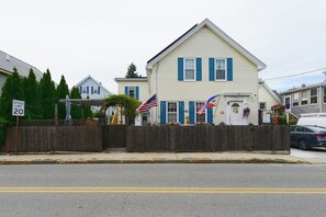 A two-story building with a gabled roof, a wooden fence, and flags. - Walk to MBTA Station! Gloucester Extended Stay (Gloucester)