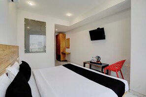 Habitació d'hotel amb llit, escriptori amb bullidora, cadira vermella i televisió penjada a la paret.