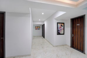 Un passadís amb parets blanques, un paviment de marbre i portes de fusta. Hi ha dues obres d'art emmarcades a les parets.