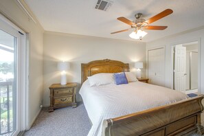 Une chambre à coucher avec un lit en bois, deux tables de chevet avec des lampes, un ventilateur de plafond et une vue sur l’extérieur par une fenêtre.