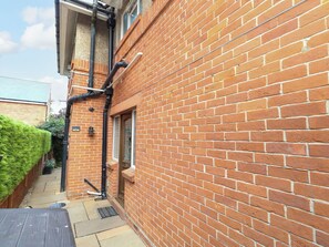 A narrow brick alleyway with a door, a window, and a black pipe running along the wall. - Coast Path Cottage (Weymouth)