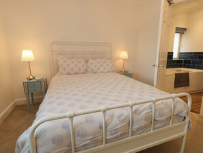 Ein Bett mit Metallgestell, zwei Nachttische mit Lampen, ein Badezimmer mit Badewanne und eine geflieste Wand.