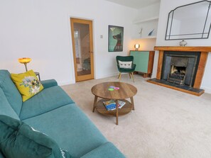 Ein Wohnzimmer mit einem türkisfarbenen Sofa, einem runden Holztisch, einem grünen Sessel, einem Kamin und einer Tür zu einem anderen Raum.