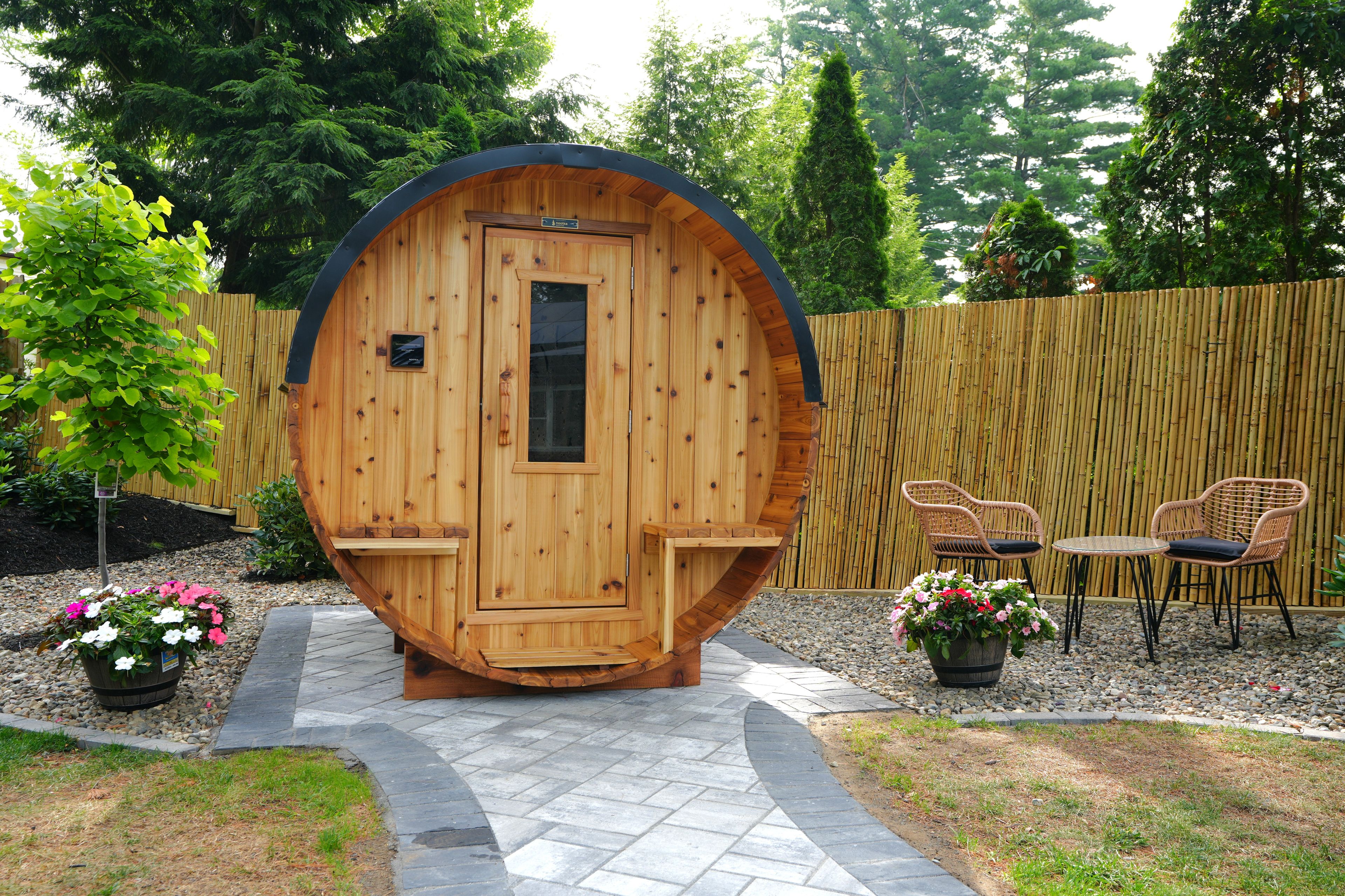 Une structure de sauna en bois, dotée d’une porte, d’un espace détente avec des chaises et une table, ainsi que de plantes en pot.