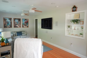 Una sala de estar con sofá, televisión, ventilador de techo y estante con adornos.