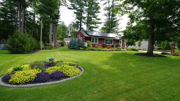 A residential property with a well-maintained lawn, a flower bed with various flowers, and a red house with solar panels.