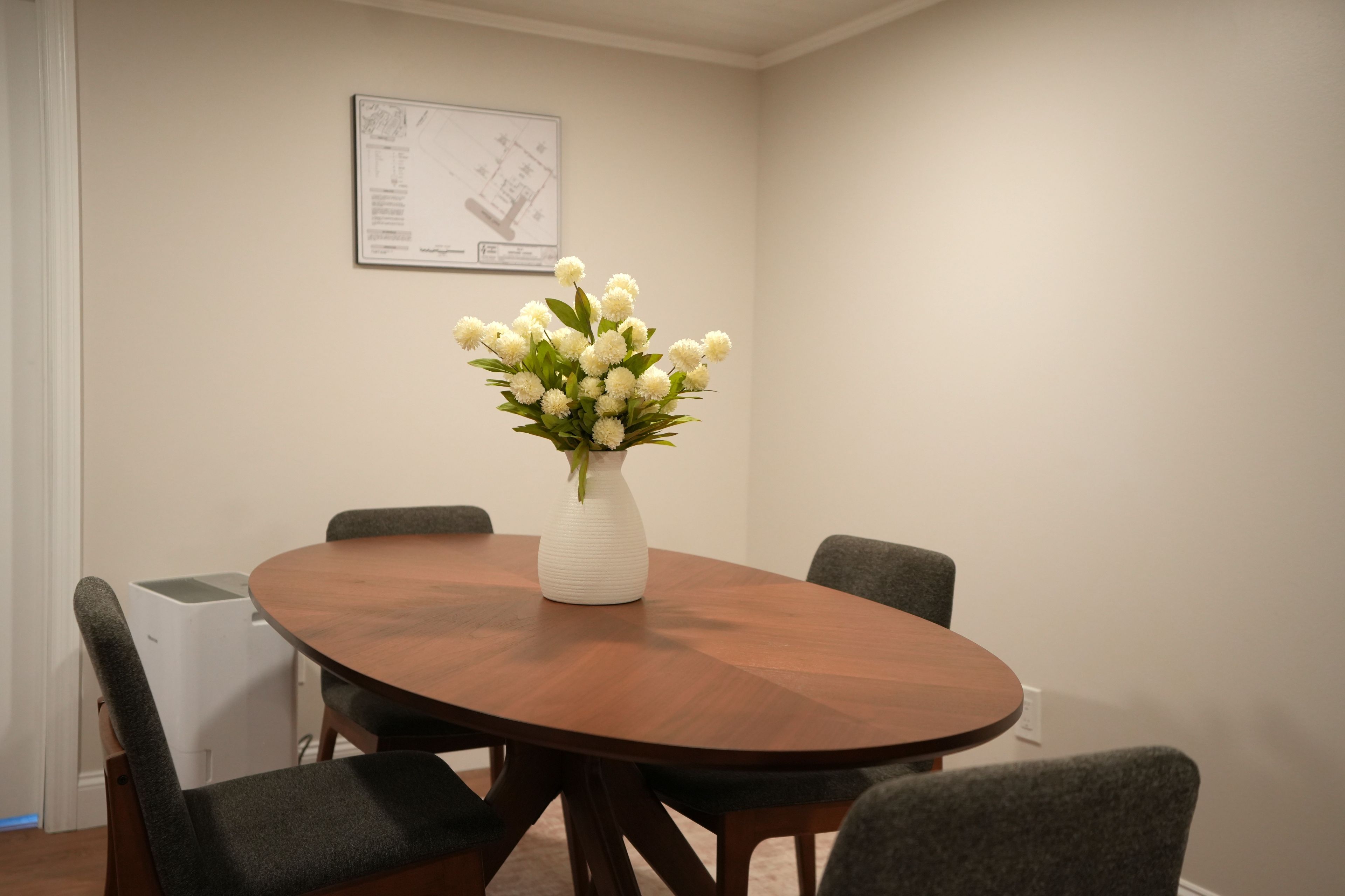 A conference room with a round wooden table, four grey chairs, and a white vase with white flowers.