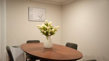 A conference room with a round wooden table, four grey chairs, and a white vase with white flowers.