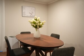 A conference room with a round wooden table, four grey chairs, and a white vase with white flowers.
