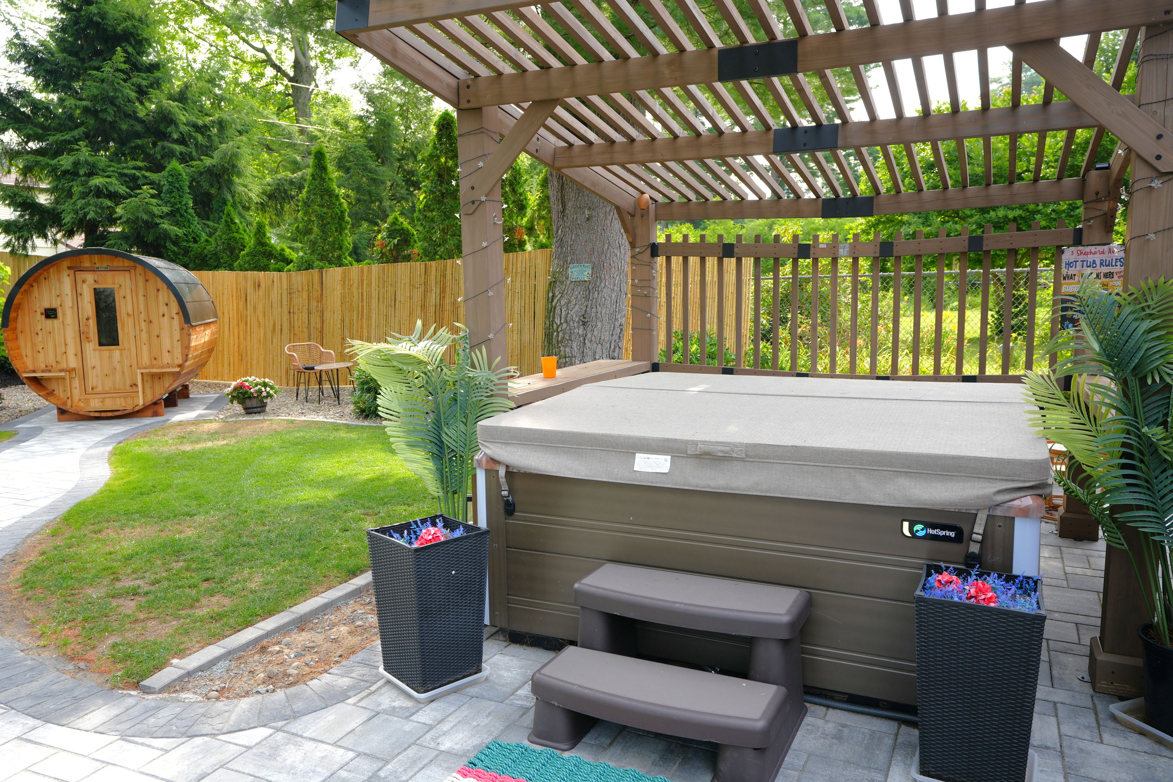 Un bain à remous avec des marches, entouré d’une pergola en bois, d’un tonneau en bois et de plantes en pot.