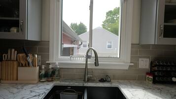 A kitchen with a sink, a window, and a view of a house outside.