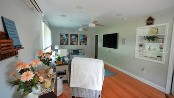 Una habitación con cama, escritorio con lámpara, televisor y estante con plantas.