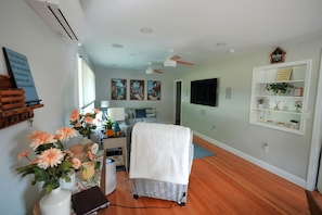 A room with a bed, a desk with a lamp, a TV, and a shelf with plants.