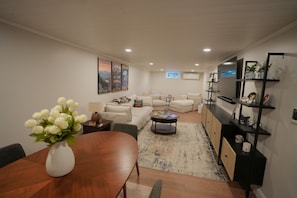 Una sala moderna con comedor, un conjunto de sofás, una mesa de centro y un televisor montado en la pared.