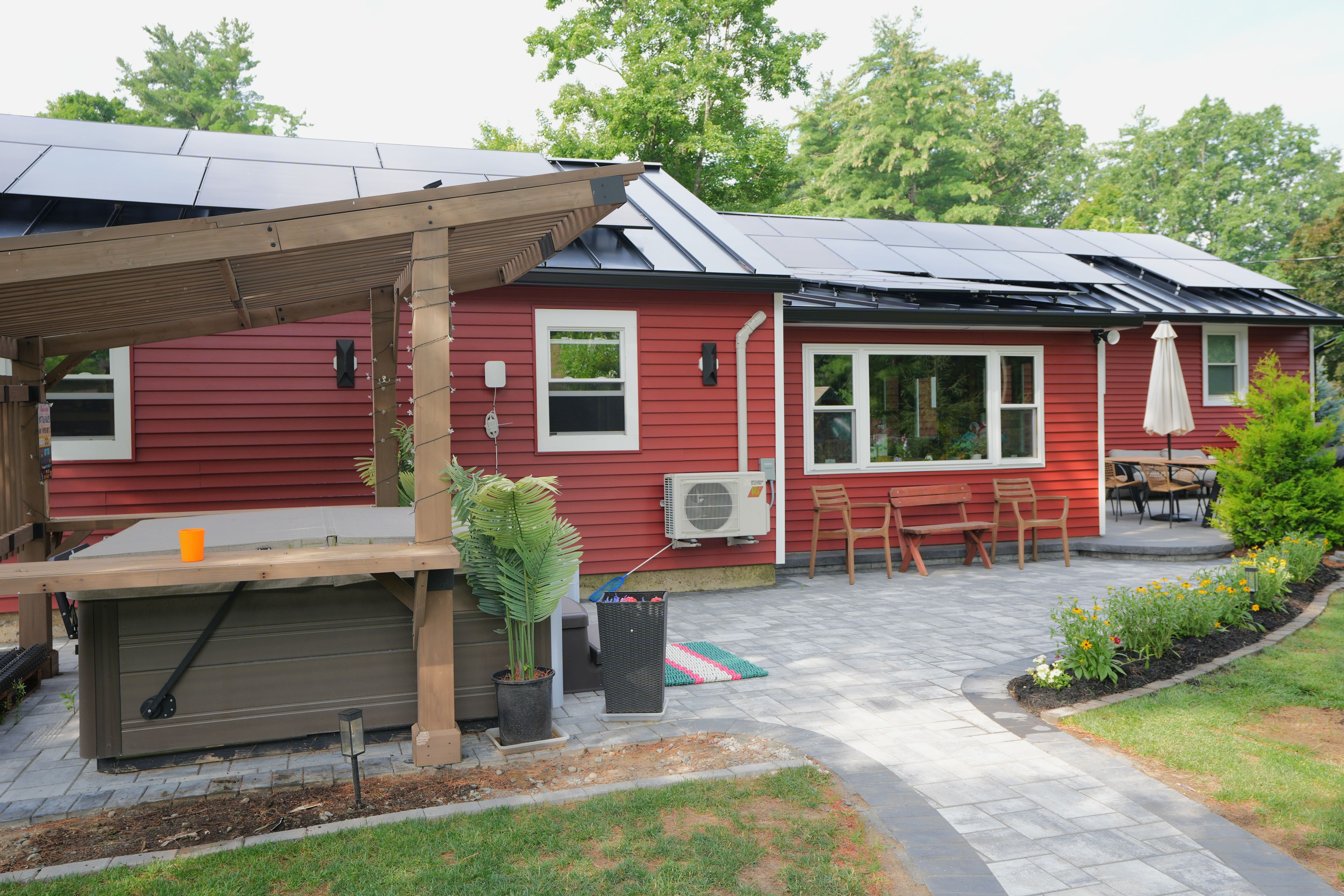Una casa roja con porche cubierto, paneles solares y jardín.