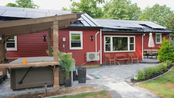 Una casa roja con porche cubierto, paneles solares y jardín.