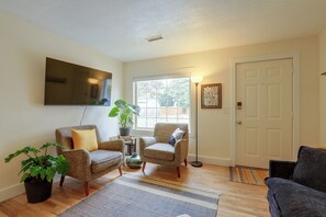 A living room with two armchairs, a coffee table, a TV mounted on the wall, a potted plant, and a door. - Quiet Neighborhood, Home Office & Fenced Yard! (Portland)
