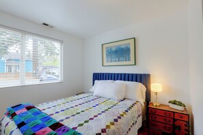 A bedroom with a bed, a window with blinds, a bedside table with a lamp, and a painting on the wall. - Quiet Neighborhood, Home Office & Fenced Yard! (Portland)