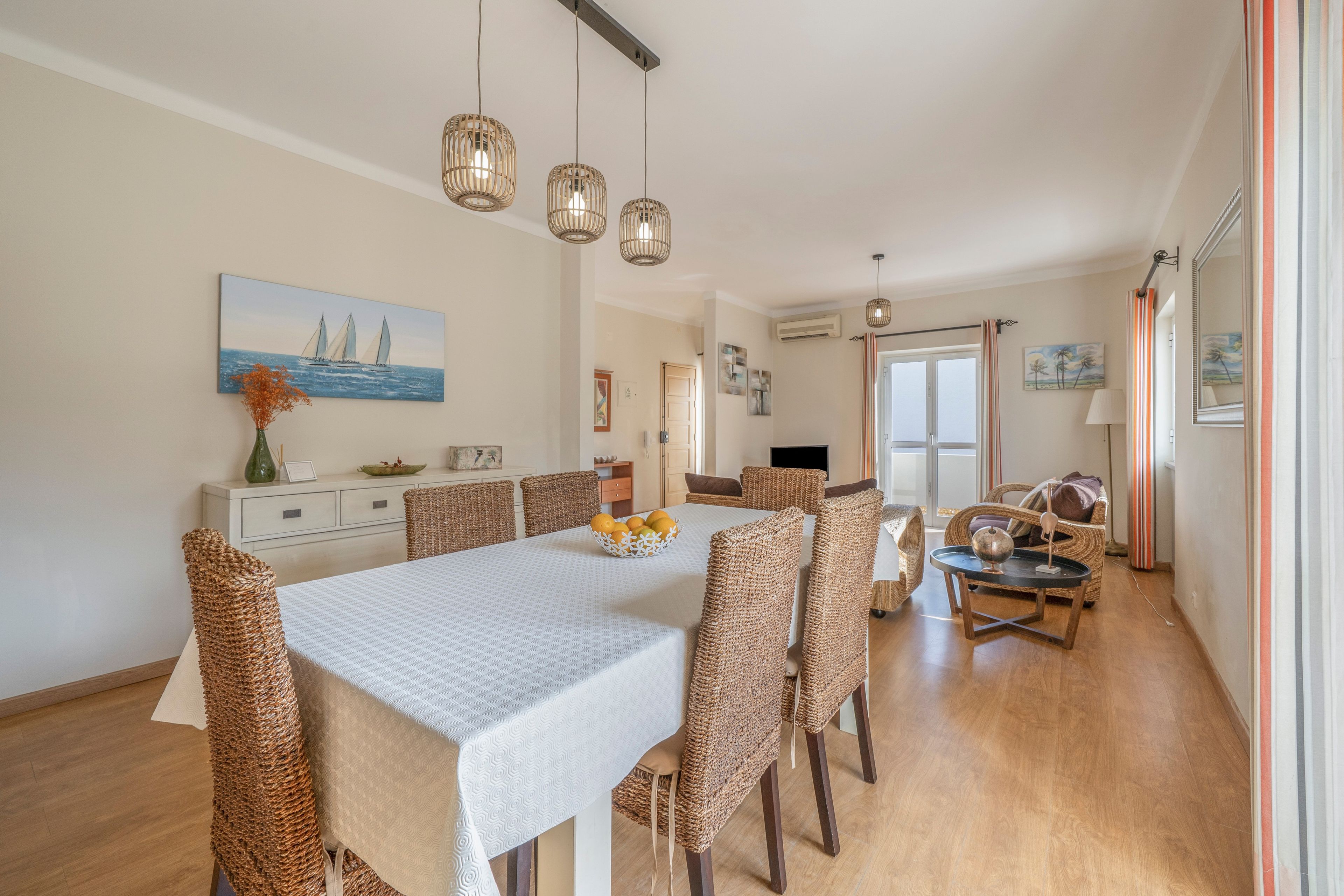 A dining area with a white table, wicker chairs, and hanging pendant lights.
