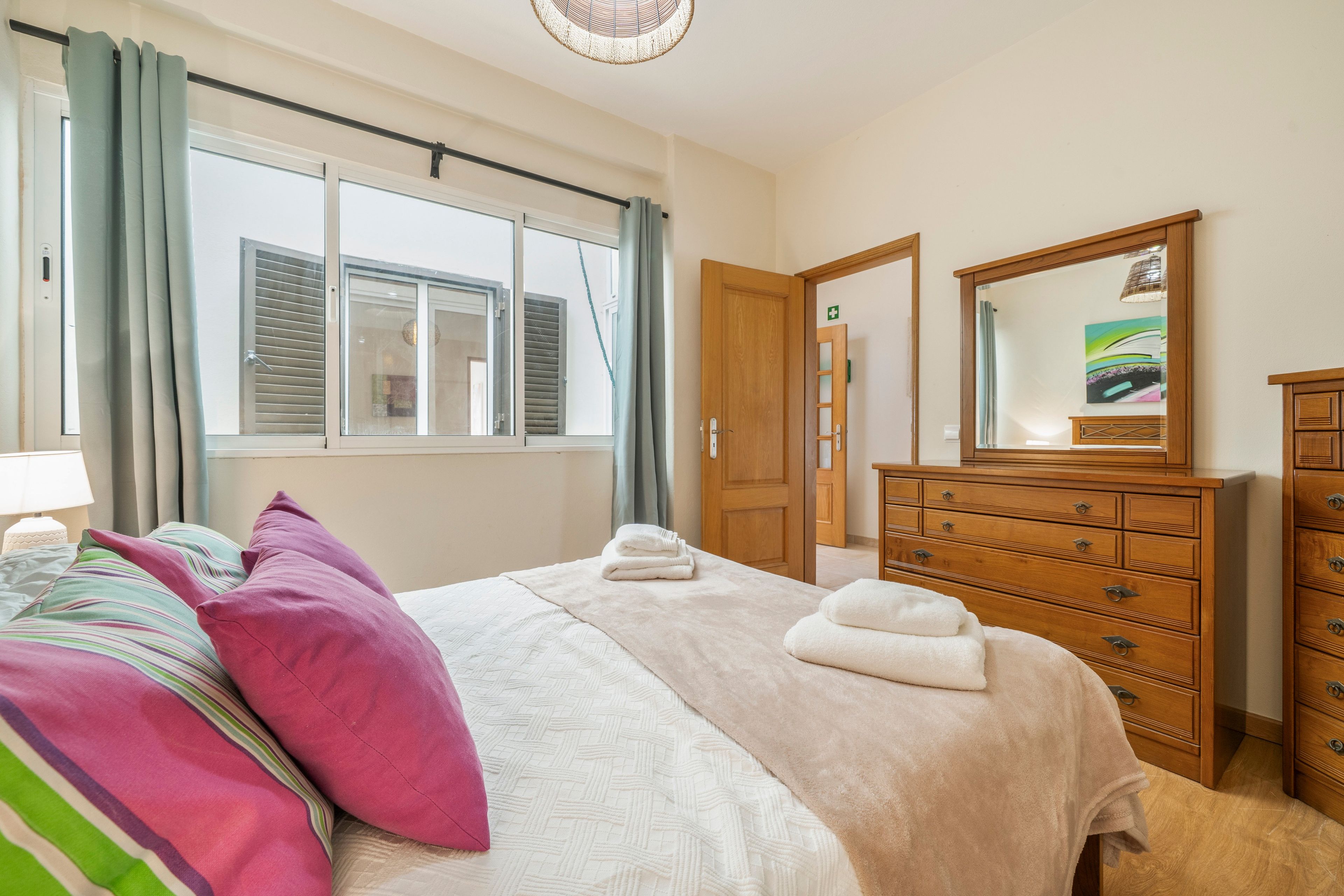 A hotel room with a bed, a dresser, a mirror, and a window with curtains.