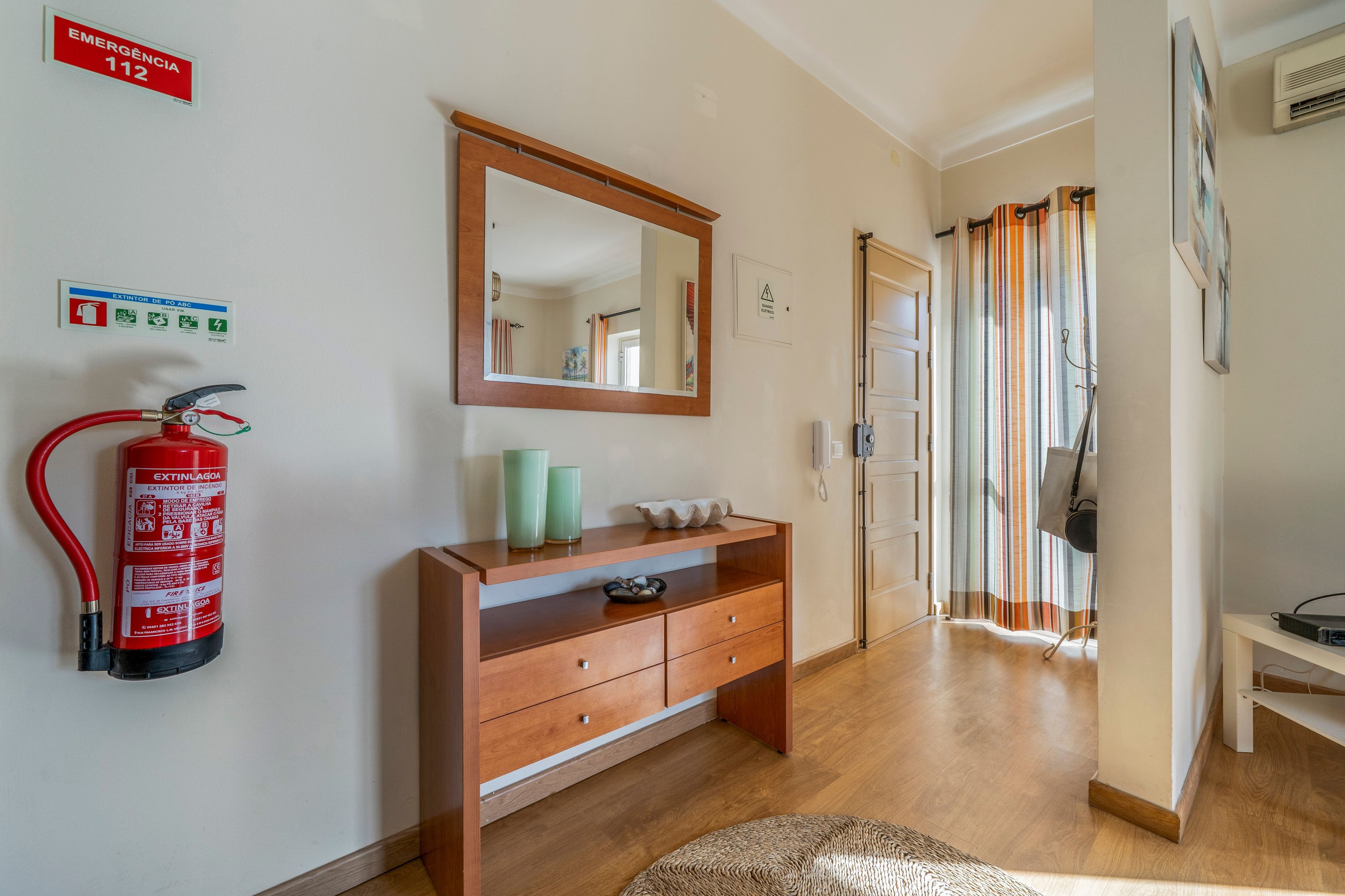 A hotel room with a wooden dresser, a fire extinguisher, a mirror, and a shower curtain.