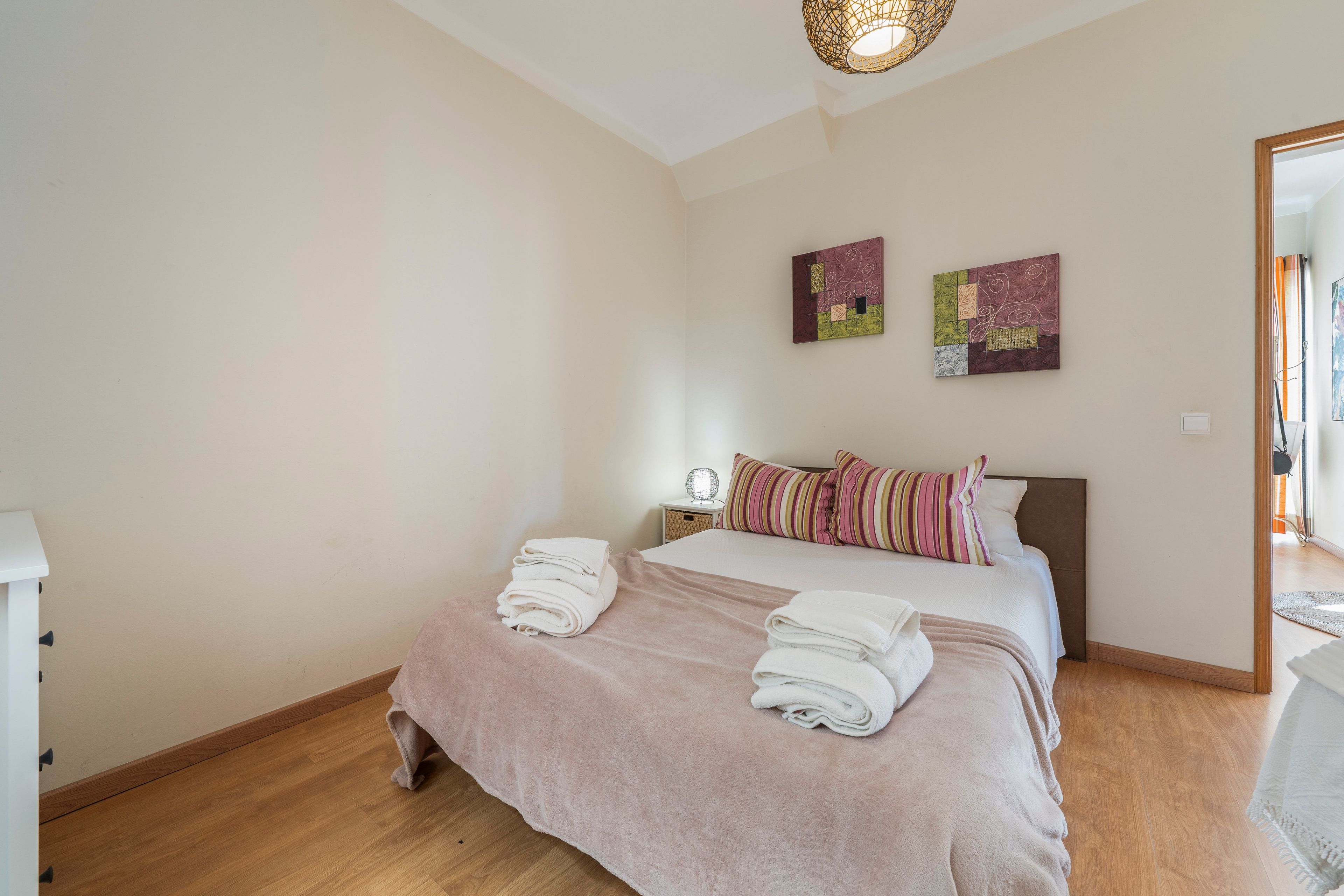 Una camera da letto con un letto, cuscini, un comodino, una lampada e un'opera d'arte a parete.