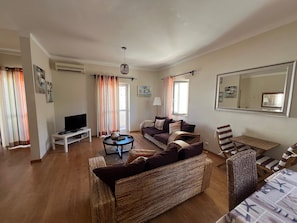 A living room with a sofa, a TV, a coffee table, and a wicker chair. - Holiday Home 'Apartamento Praia' with Sea View, Wi-Fi and Air Conditioning (Armação de Pêra)