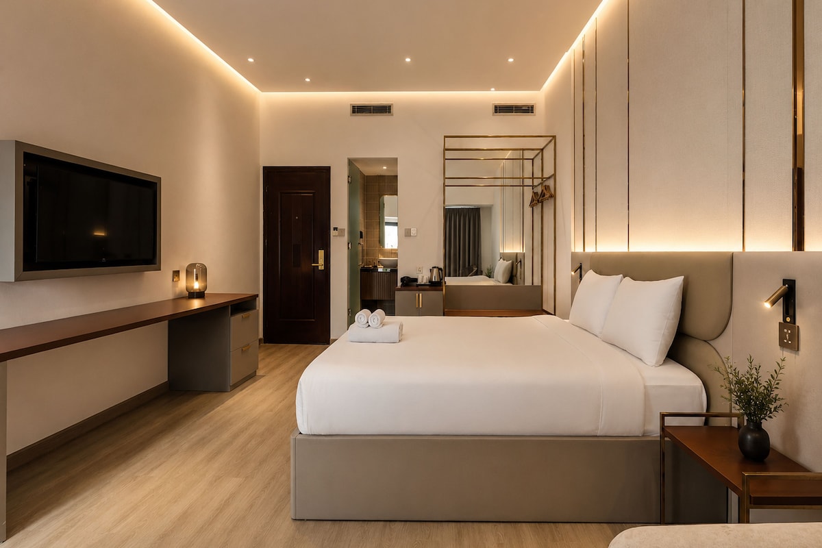 A modern hotel room with a large bed, bedside tables, a flat-screen TV, and a bathroom visible through an open door.