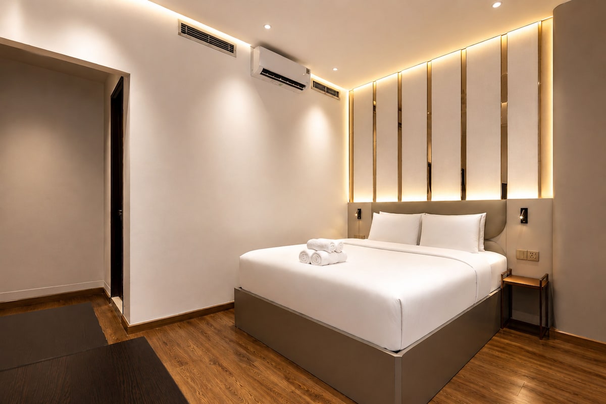 A modern hotel room with a large bed, a bedside table, a wall-mounted air conditioner, and a wooden floor.