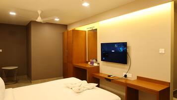 Quarto de hotel com cama, escrivaninha, televisão e armário.