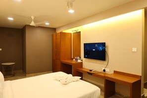 Quarto de hotel com cama, escrivaninha, televisão e armário.