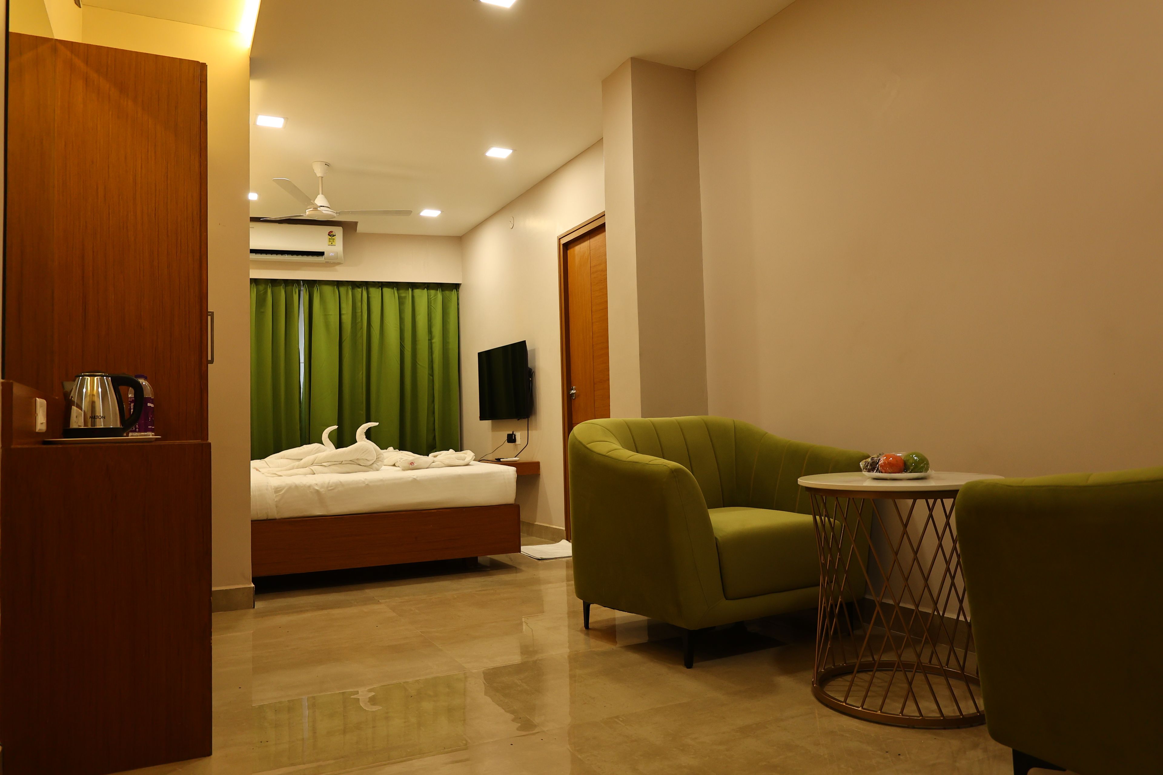 A hotel room with a bed, a green armchair, a small round table, and a television.