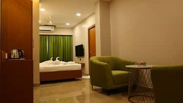 A hotel room with a bed, a green armchair, a small round table, and a television.