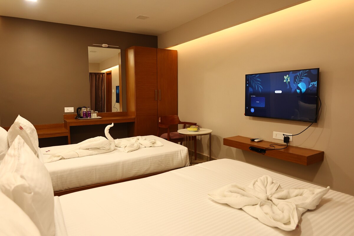 A hotel room with two beds, a TV, a small table, a mirror, and a wardrobe.