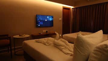 Quarto de hotel com cama, poltrona, mesa pequena, televisão na parede e porta.
