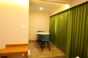 Una habitación pequeña con una mesa redonda y sillas, un banco de madera y una cortina verde.