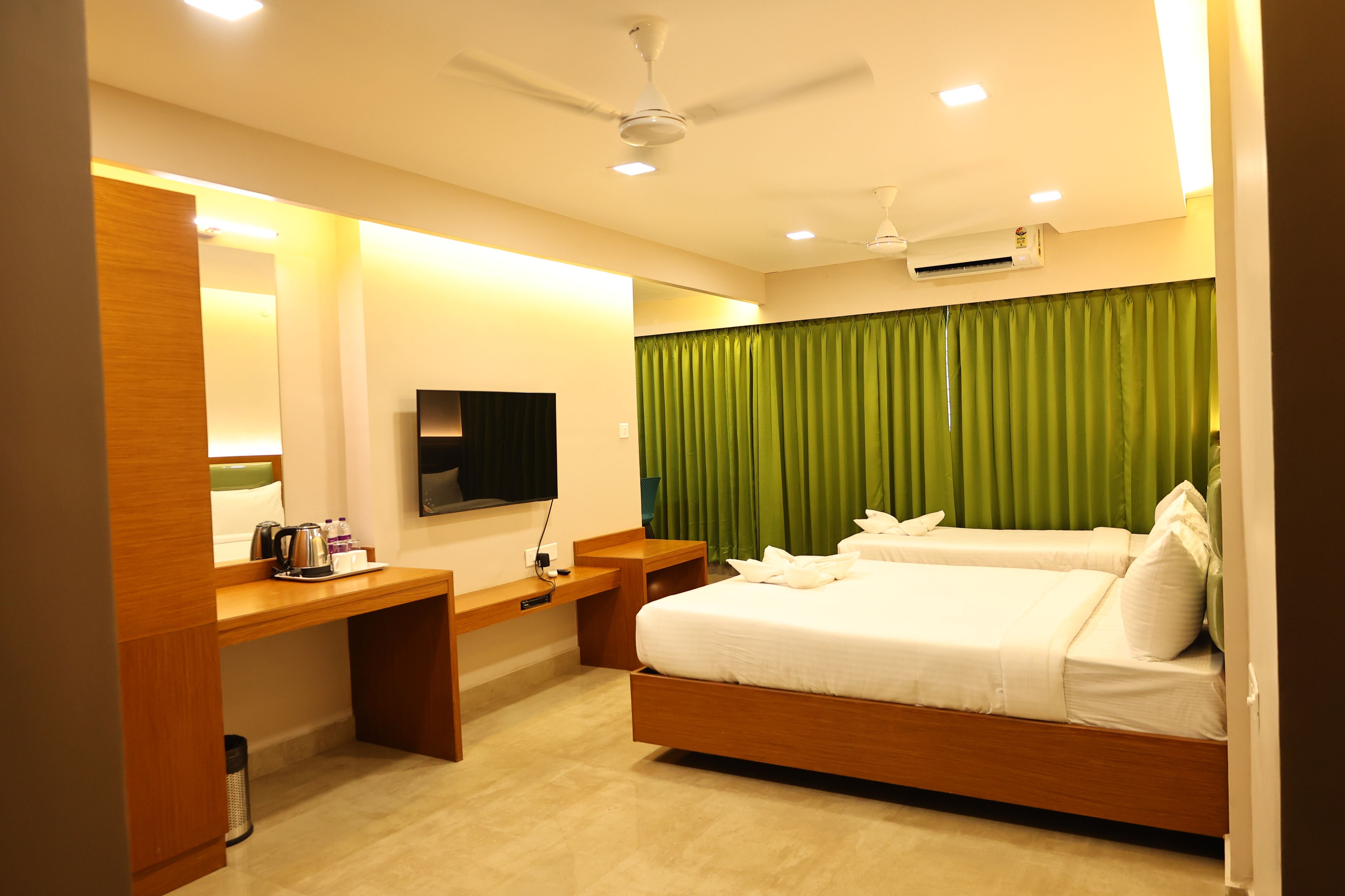 Quarto de hotel com cama, escrivaninha, televisão e ventoinha no teto.