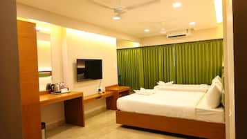 Quarto de hotel com cama, escrivaninha, televisão e ventoinha no teto.