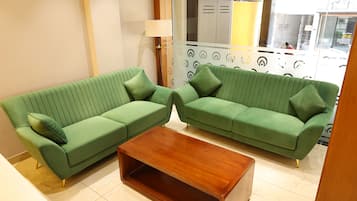 Um quarto com dois sofás verdes, uma mesa de centro de madeira e uma parede estampada.