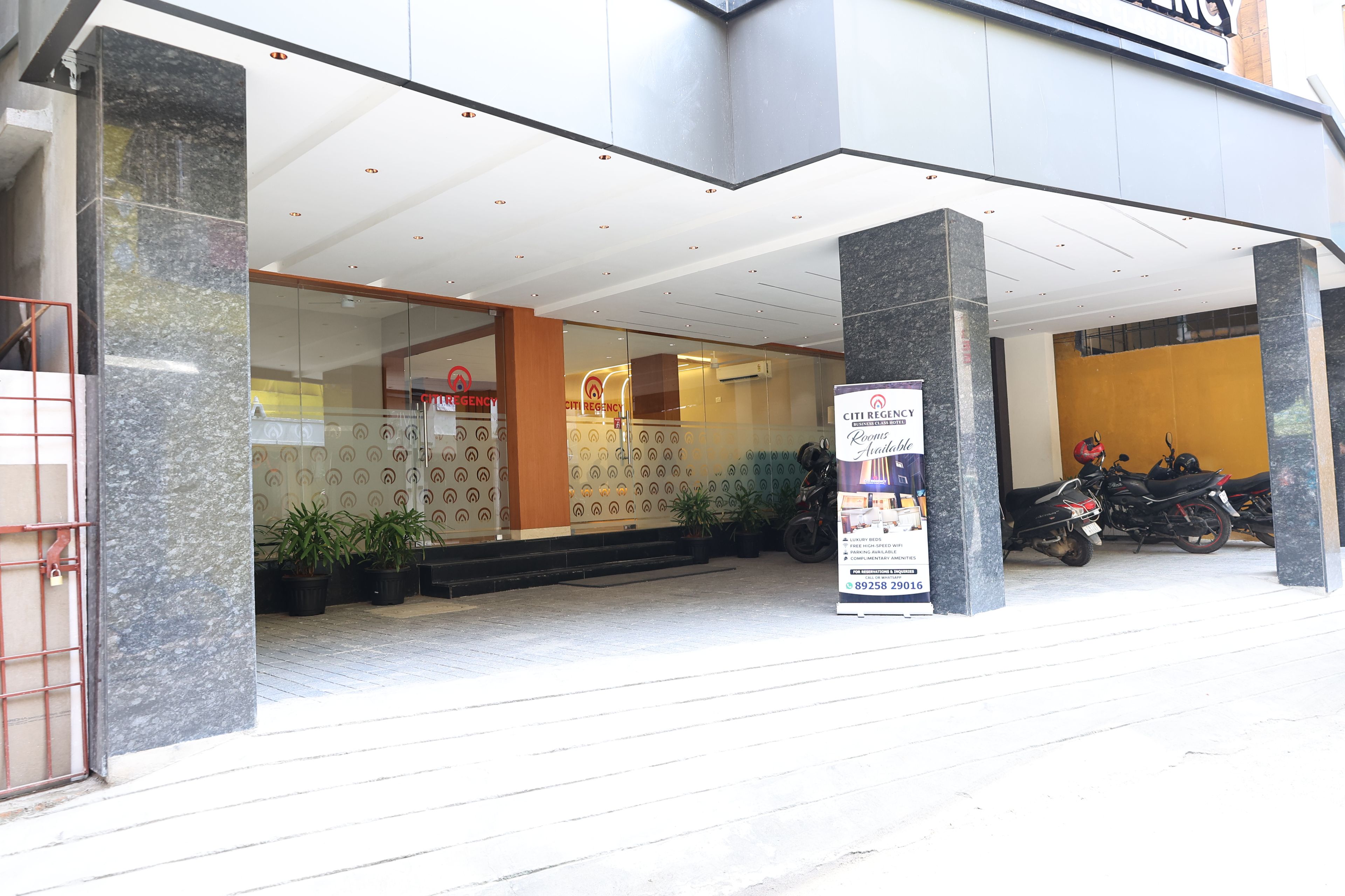 Entrada de hotel com fachada de vidro, placa de identificação e uma motocicleta estacionada.