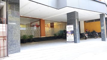 Entrada de hotel com fachada de vidro, placa de identificação e uma motocicleta estacionada.