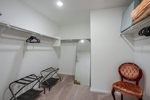 A walk-in closet with a mirror, a chair, and a shelf with hangers.